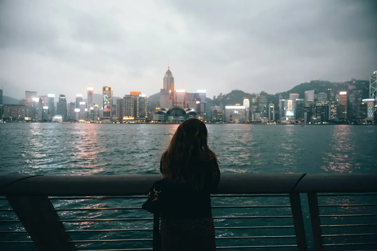 Una ragazza sul lungomare di Tsim Sha Tsui guarda lo skyline dell'isola di Hong Kong
