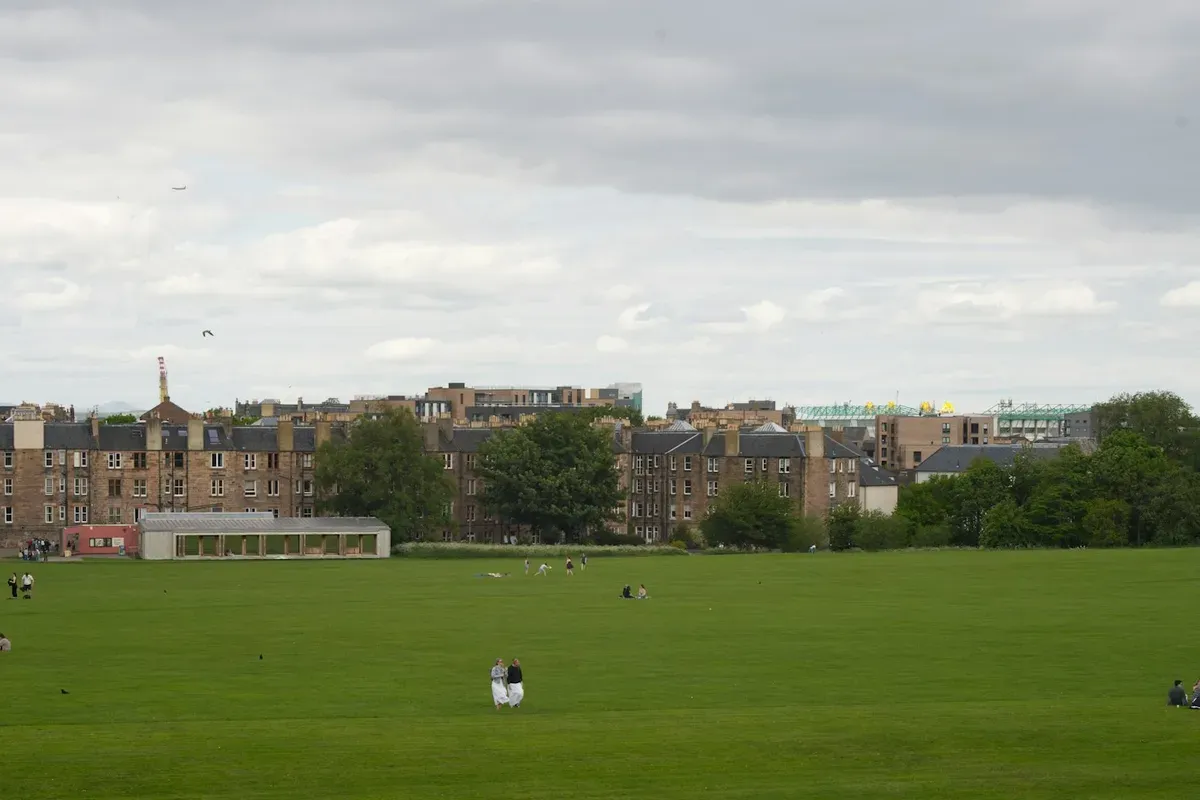 Un grande prato verde in un parco di Edimburgo, con le case di pietra sullo sfondo