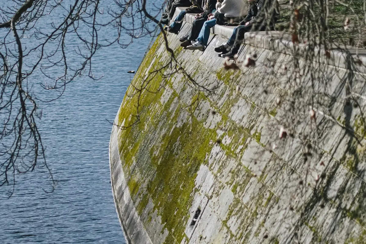 Persone sedute sul muro lungo il Landwehrkanal a Berlino, sopra l'acqua