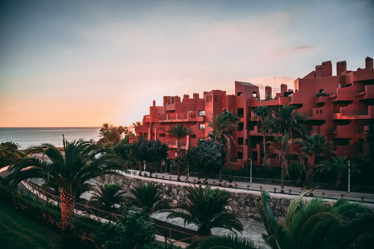 Un albergo rosso con le palme sul lungomare della Costa Adeje al tramonto