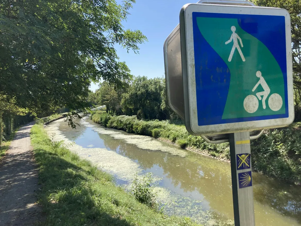 Un canale con il cartello di una pista ciclopedonale sulla sponda