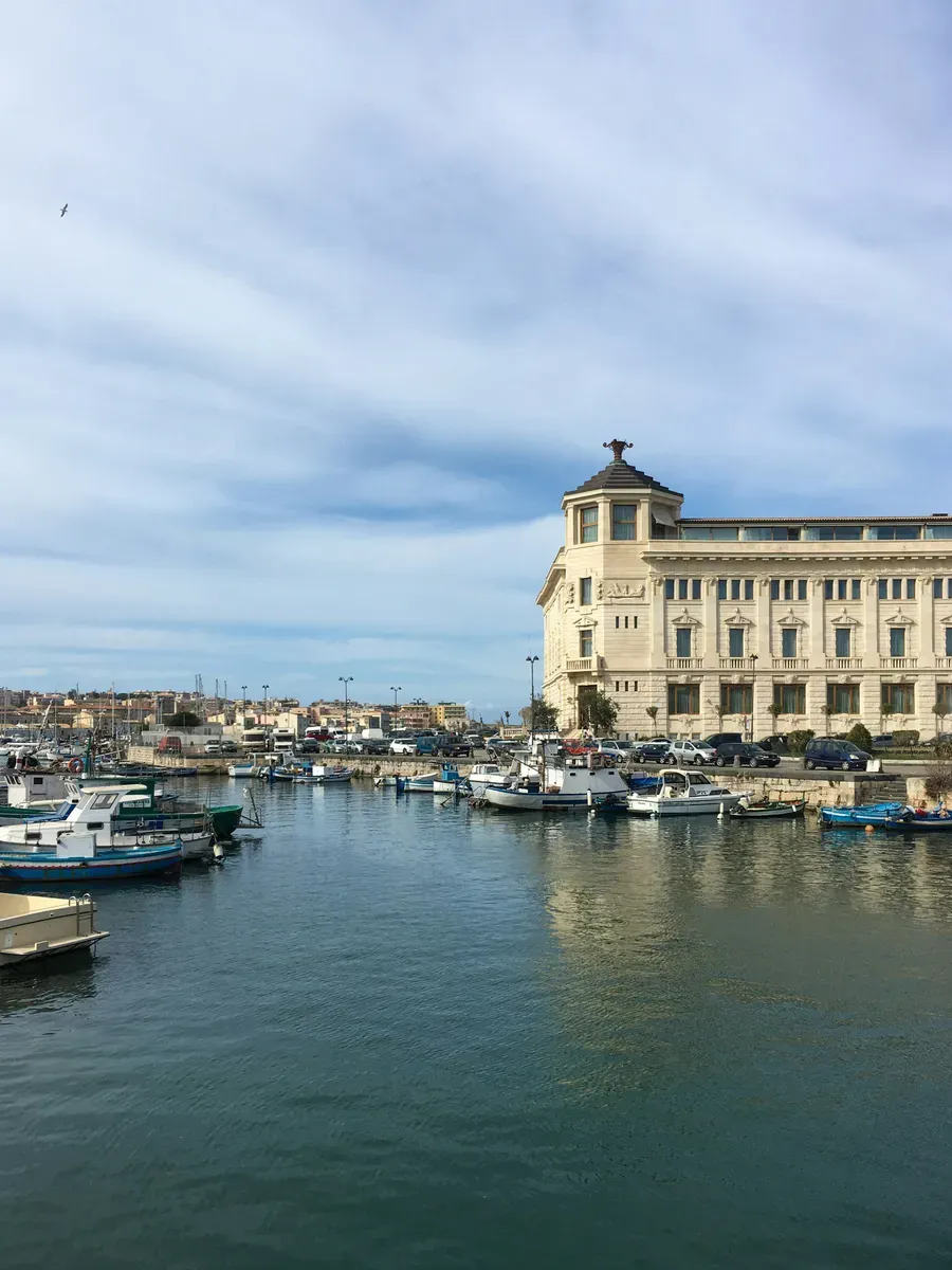 Barche ormeggiate in un porto siciliano, con un palazzo storico sul molo
