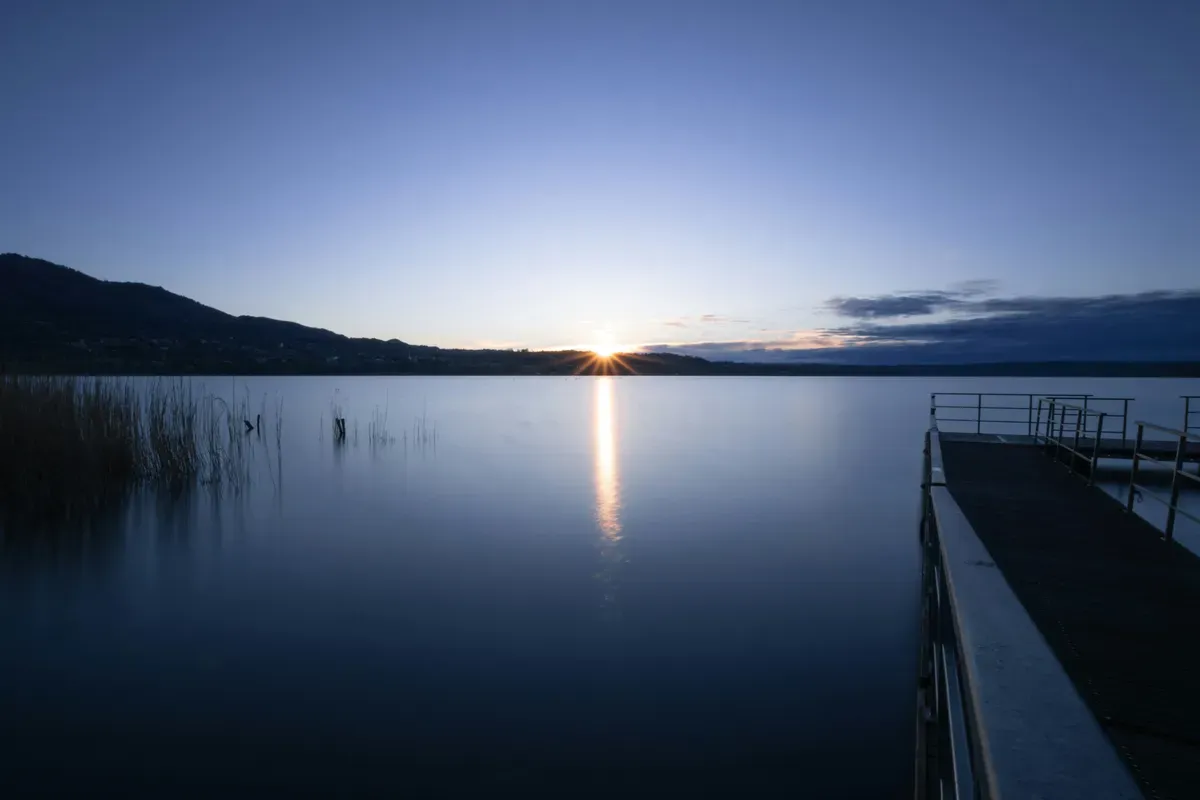 Il sole che tramonta dietro le colline sul lago, con un pontile