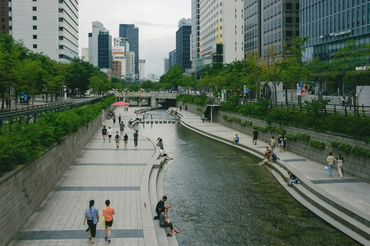 Persone che camminano lungo il torrente Cheonggyecheon tra i grattacieli del centro di Seul