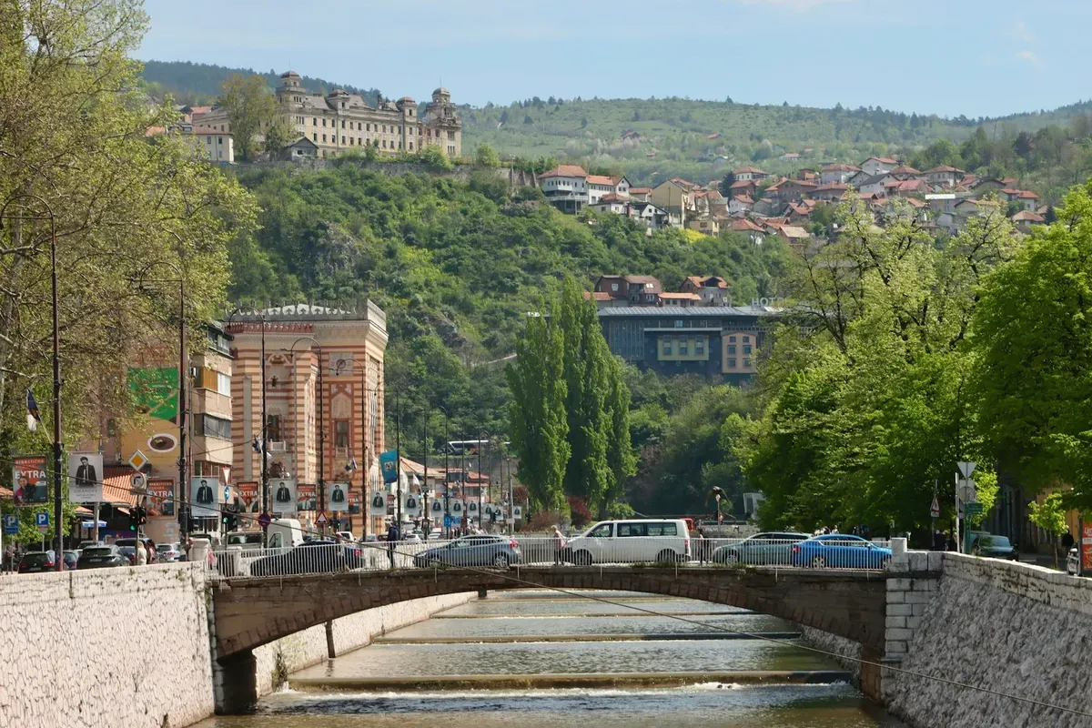 La Miljacka e uno dei suoi ponti nel centro di Sarajevo, con la Vijećnica e le colline sullo sfondo