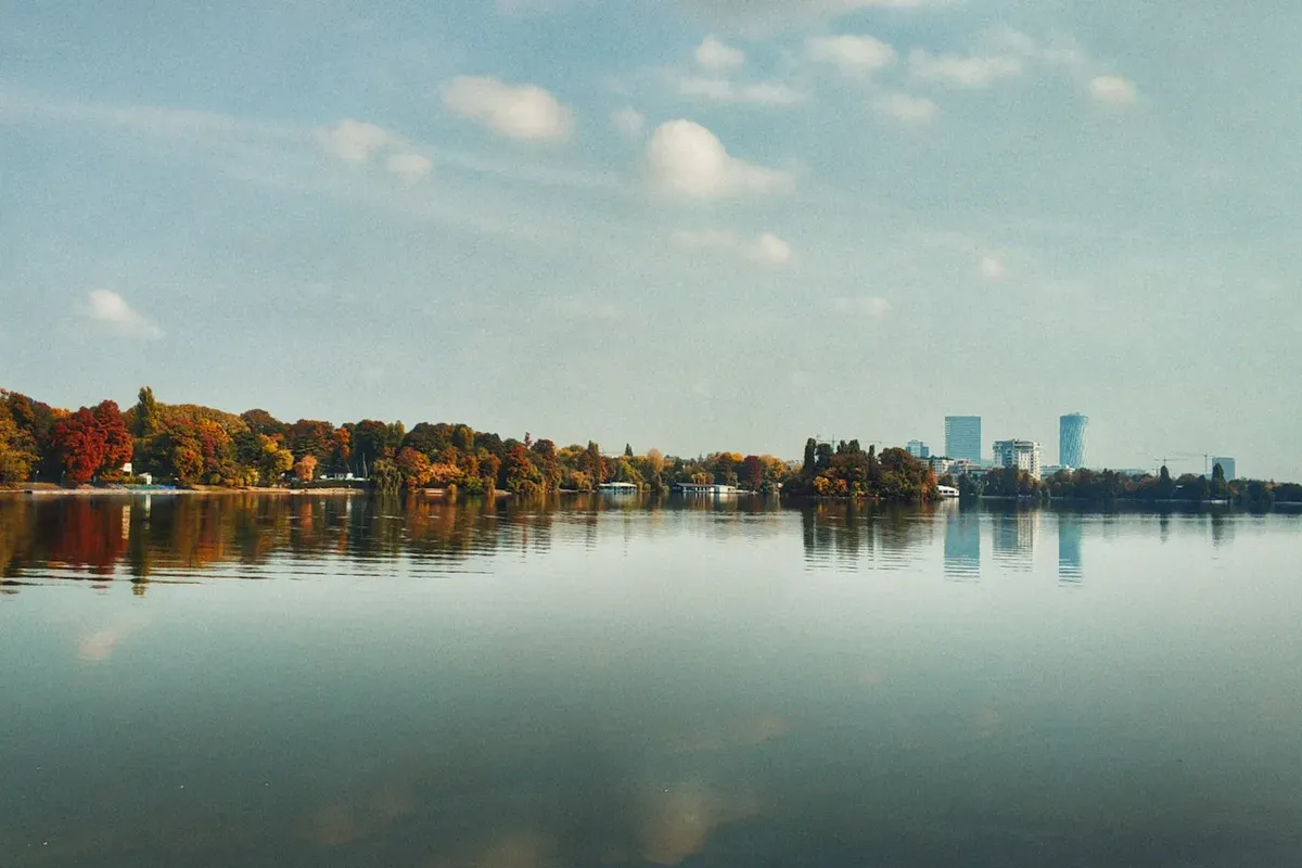 Il lago Herăstrău in autunno, con gli alberi colorati sulla riva e i grattacieli di Bucarest sullo sfondo