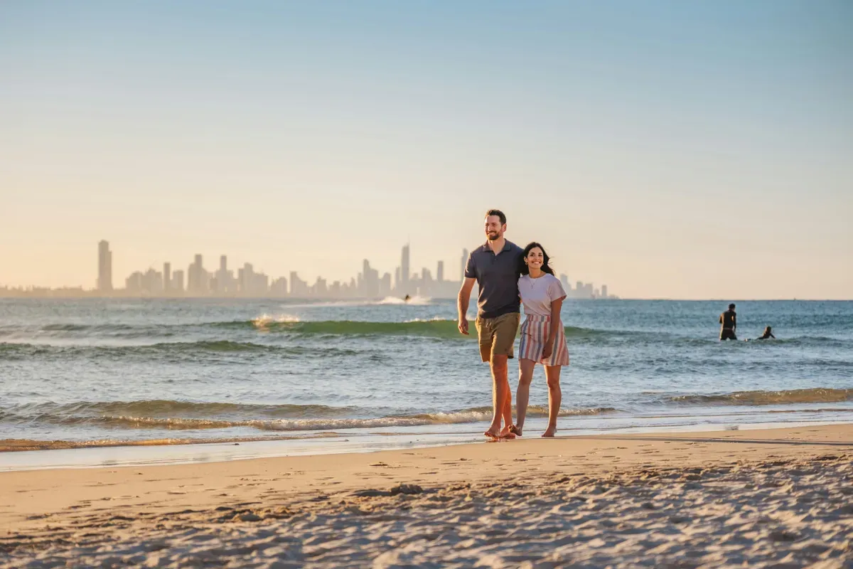Due persone che camminano sulla spiaggia, con lo skyline della Gold Coast lontano