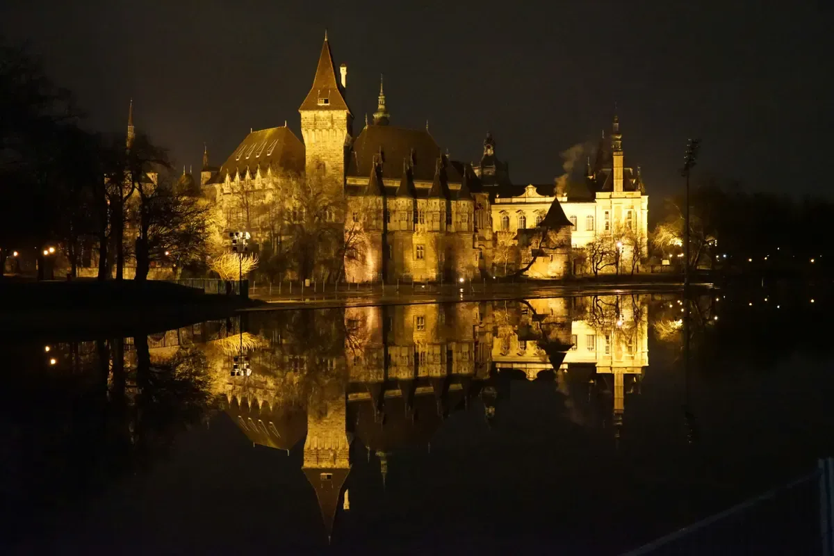 Il castello di Vajdahunyad illuminato di notte che si riflette nel lago del Városliget