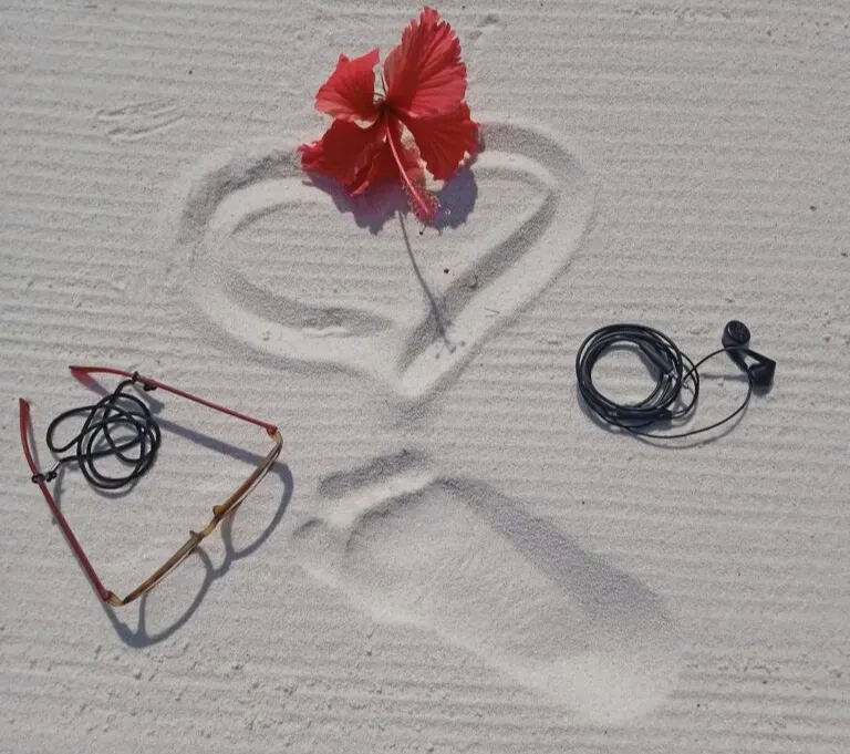 Un cuore disegnato sulla sabbia con un fiore di ibisco, occhiali da sole e auricolari