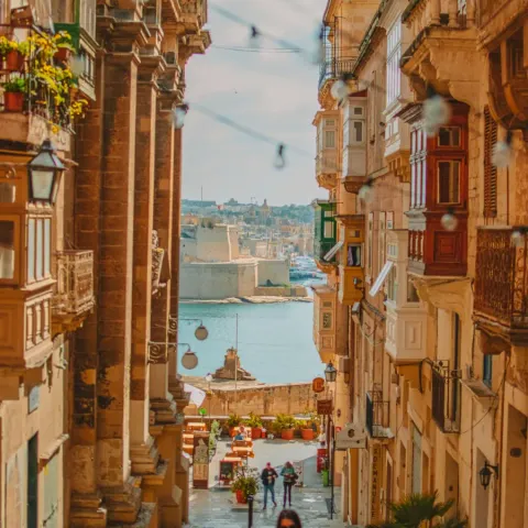 Una via in salita di La Valletta con i balconi colorati e il mare in fondo