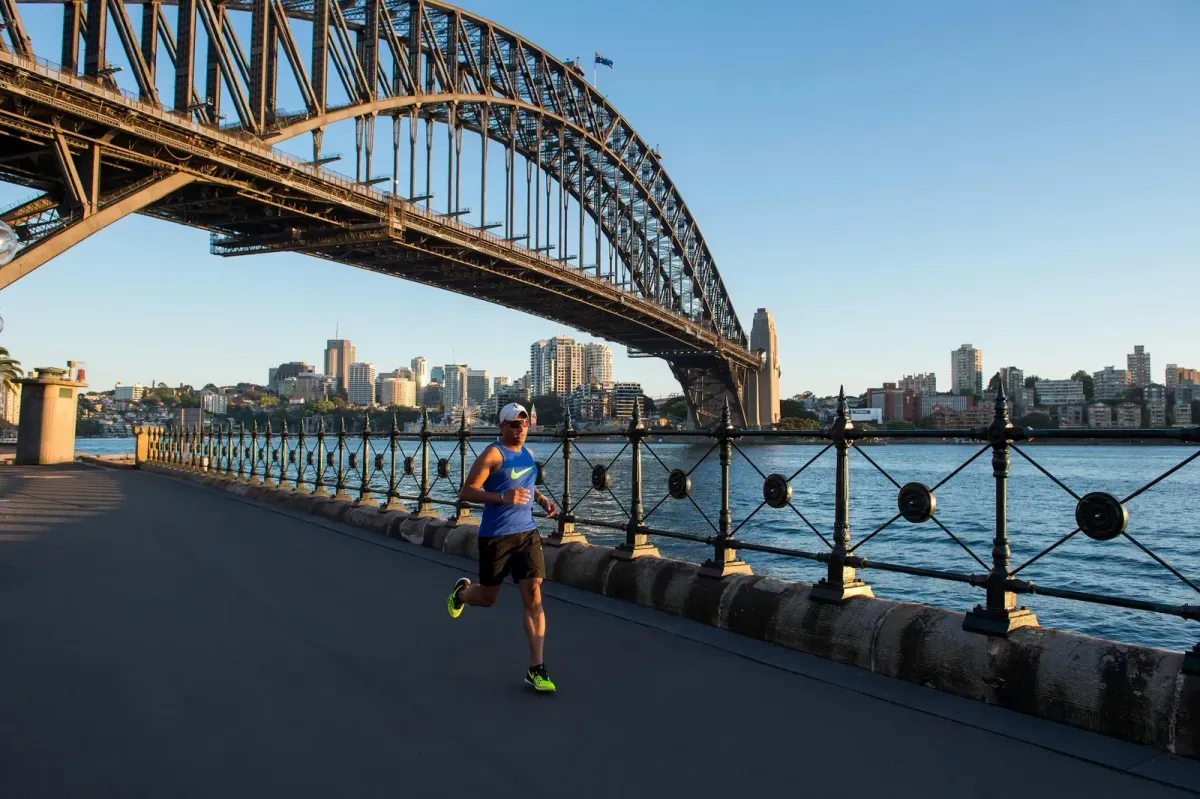 Un runner corre sul lungomare di Sydney sotto l'Harbour Bridge