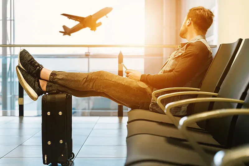 Un ragazzo con i piedi sulla valigia aspetta in aeroporto mentre un aereo decolla