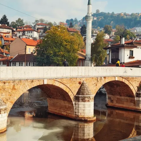 Un ponte ottomano in pietra sulla Miljacka a Sarajevo, con le case e un minareto sulla collina