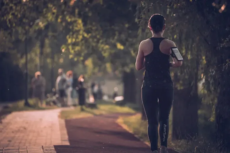 Una runner di spalle corre in un viale alberato al tramonto