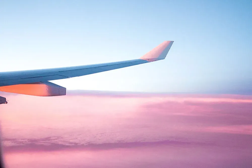 L'ala di un aereo sopra le nuvole rosa al tramonto